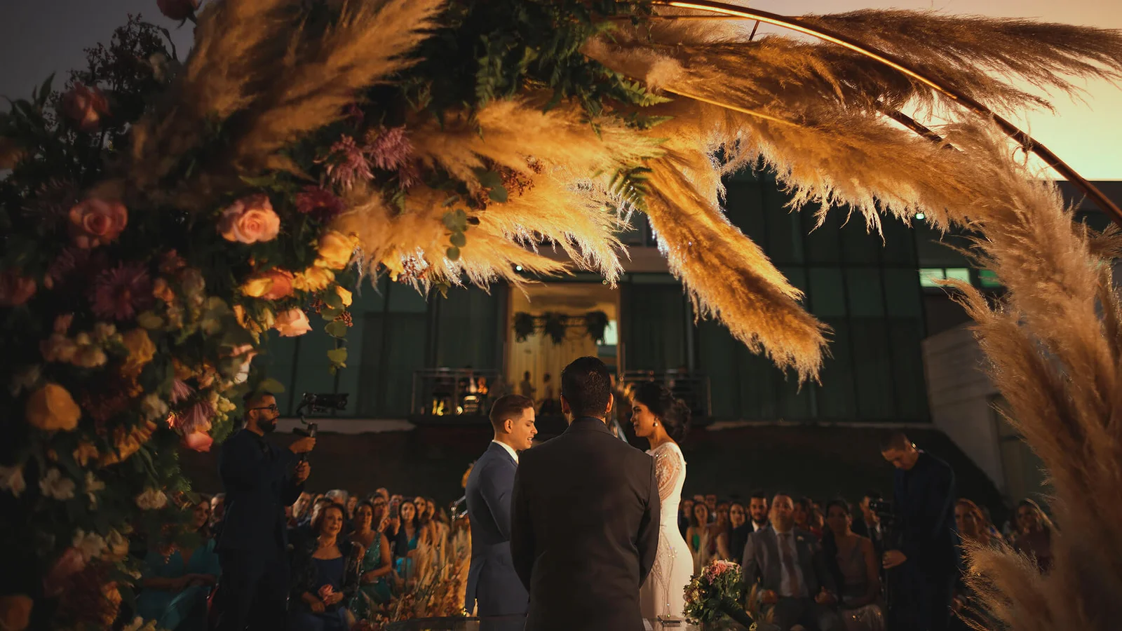 Cerimônia de casamento ao pôr do sol sob arco de pampas na área verde do Green Place